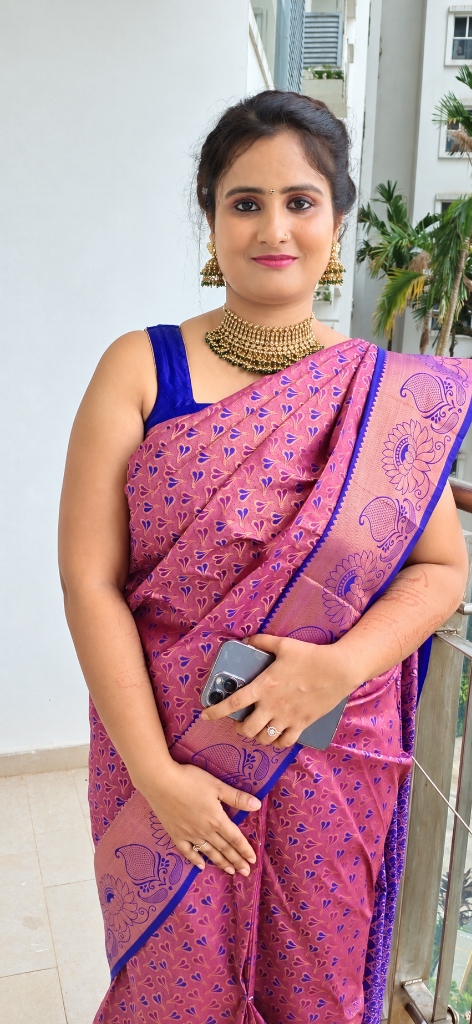 Festive pink silk saree draping with royal blue contrast, gold choker, and matching jhumkas